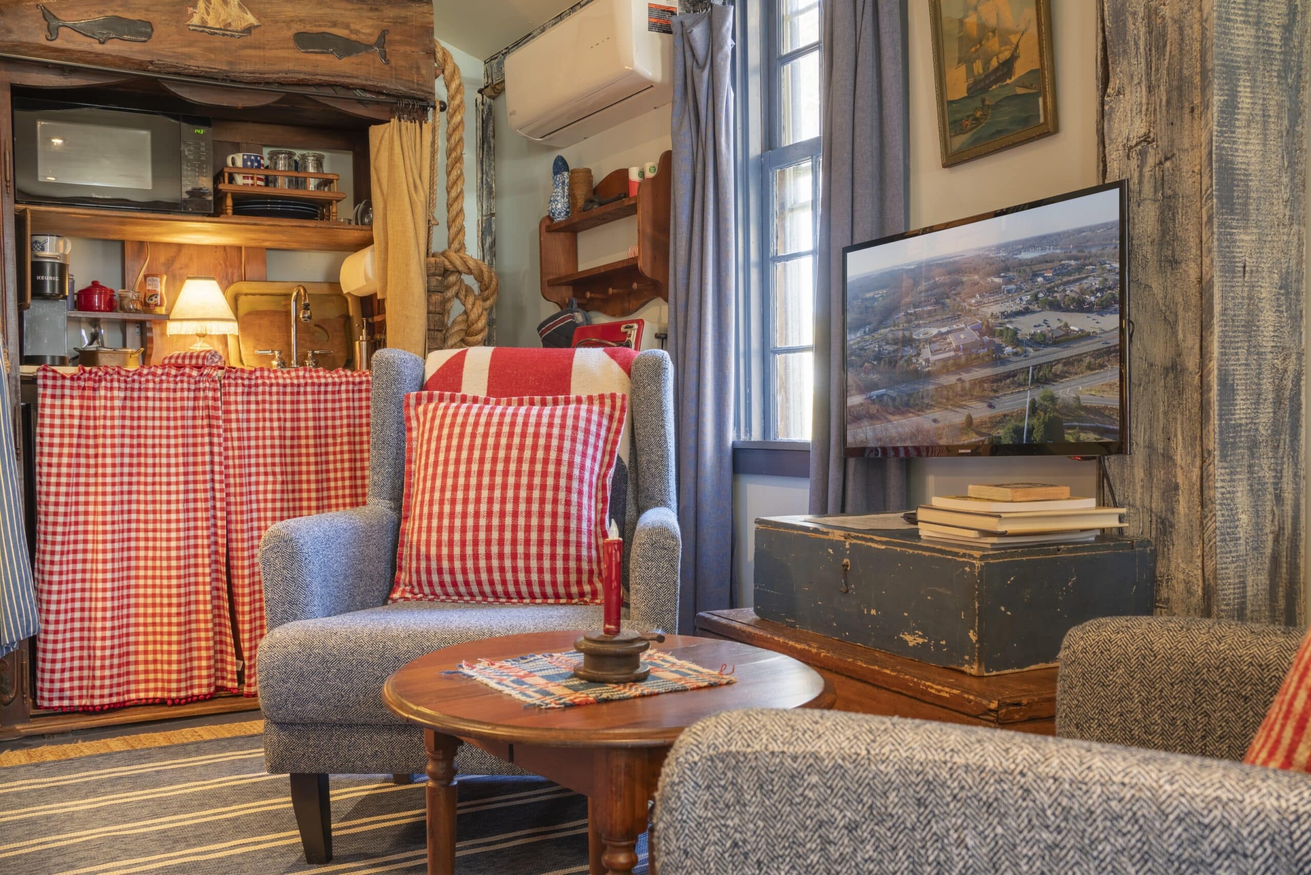 Cozy living room perfect for short term rental photography in Waterford Connecticut, featuring checkered red-and-white curtains, a blue armchair, rustic decor, a round wooden table with a candle, and a welcoming ambiance.